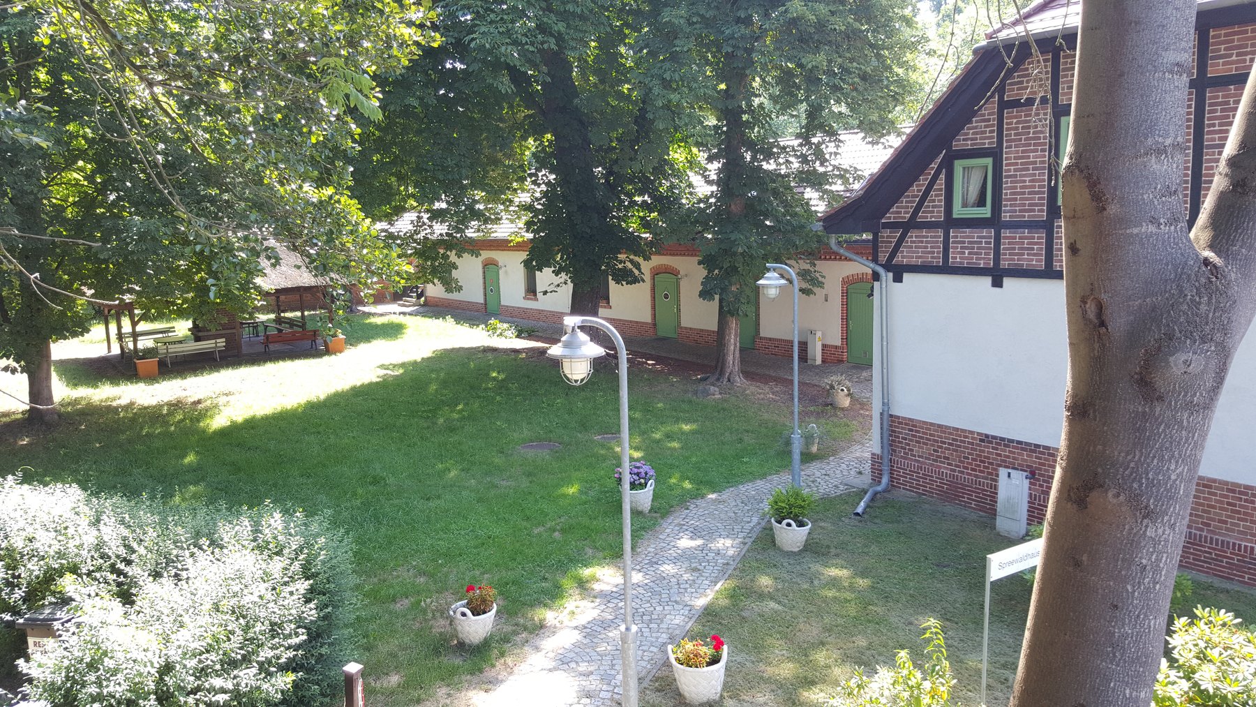 Blick über das Hofgelände mit Wiese, altem Baum und dem Fachwerkgebäude